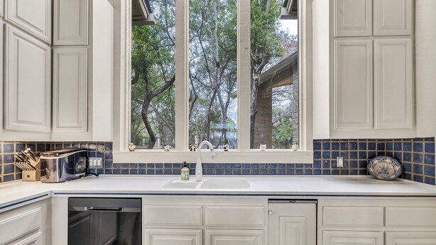 A kitchen with white cabinets, a window with a view of trees, a sink, and a dish rack. - Luxury Austin Estate – Tranquil, Spacious & Packed with Games and Pool. (Austin)