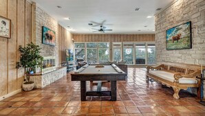 A spacious room with a pool table, wooden benches, and large windows. - Luxury Austin Estate – Tranquil, Spacious & Packed with Games and Pool. (Austin)