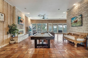 Una habitación amplia con mesa de billar, bancos de madera y ventanas grandes.