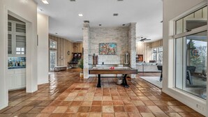 A spacious room with a pool table, a stone accent wall, and large windows. - Luxury Austin Estate – Tranquil, Spacious & Packed with Games and Pool. (Austin)