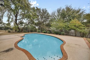Piscina com borda de deck de madeira, cercada por árvores e uma cerca.
