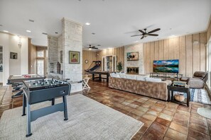 A spacious living room with a foosball table, a sofa, a TV, and a fireplace. - Luxury Austin Estate – Tranquil, Spacious & Packed with Games and Pool. (Austin)