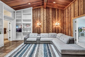 A modern living room with a sectional sofa, wooden panel walls, and built-in shelving. - Luxury Austin Estate – Tranquil, Spacious & Packed with Games and Pool. (Austin)