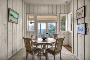 A dining area with a round wooden table and chairs, a bowl in the center, and framed artwork on the walls.