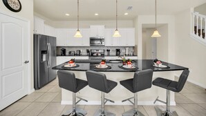 Una cocina moderna con armarios blancos, un refrigerador de acero inoxidable, una isla central con taburetes de bar e iluminación colgante.