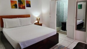 A bedroom with a bed, bedside lamp, and artwork on the wall. - Tropical Apartments Tobago : Coral Apt (Carnbee)