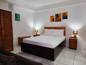 A bedroom with a bed, two bedside tables, a wardrobe, and three wall-mounted paintings.