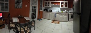 Una cocina con gabinetes blancos, una mesa de comedor con sillas y un refrigerador.