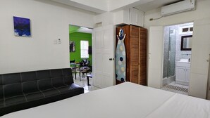 A bedroom with a large bed, a black sofa, a wardrobe, and a bathroom visible through an open door. - Tropical Apartments Tobago : Palm Apt 2 (Carnbee)