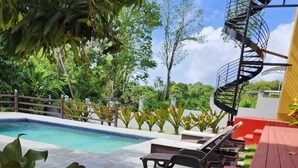 A poolside area with a spiral staircase, lounge chairs, and a red deck. - Tropical Apartments Tobago: Bluebell Apt (Carnbee)