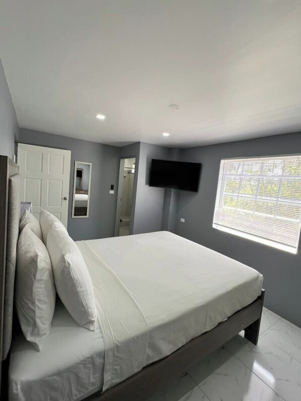 Une chambre à coucher avec un lit, un téléviseur fixé au mur et une fenêtre avec des stores.