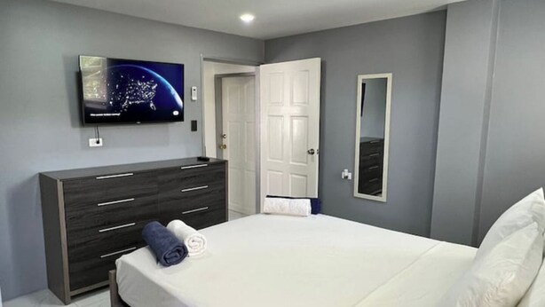 A bedroom with a bed, a dresser, a television, and a door. - Tropical Apartments Tobago: Bluebell Apt (Carnbee)