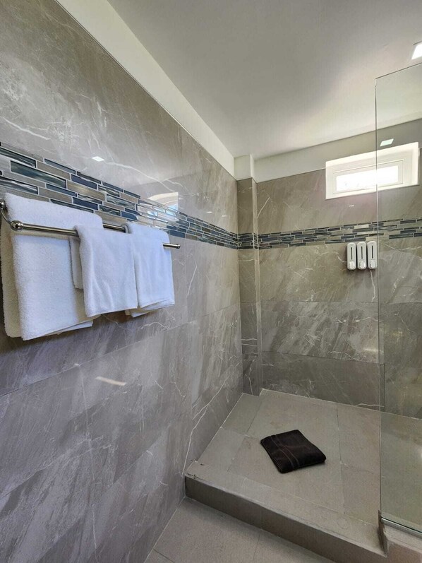 A modern bathroom with a glass shower enclosure, a towel rack with white towels, and a small black bath mat.