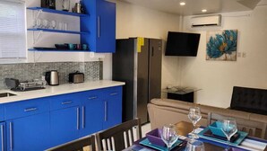 A modern kitchen with blue cabinets, a dining area with a table set for four, and a flat-screen TV mounted on the wall. - Tropical Apartments Tobago: Bluebell Apt (Carnbee)