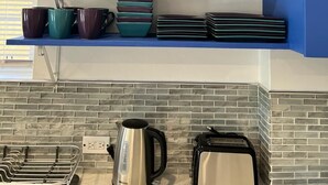 A kitchen with blue cabinets, a coffee maker, and various glassware and dishes. - Tropical Apartments Tobago: Bluebell Apt (Carnbee)