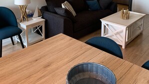 A modern living room with a dark grey sofa, a wooden coffee table, and a blue armchair. A white side table with a lamp and a decorative item is also visible.