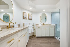 Ein geräumiges Badezimmer mit einem großzügigen Waschtisch, goldenen Armaturen und einem großen Spiegel.