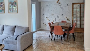A living room with a grey sofa, a dining area with a wooden table and orange chairs, and a tiled floor. - Apartment with private courtyard and parking in Sarlat town center (Sarlat-la-Canéda)