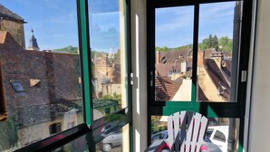 A balcony with a chair, large windows, and a view of buildings. - Apartment with private courtyard and parking in Sarlat town center (Sarlat-la-Canéda)