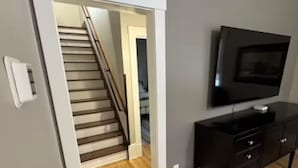 Un salon moderne avec un plancher en bois, un escalier, un téléviseur à écran plat et un meuble de rangement pour appareils électroniques de couleur sombre.