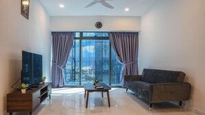 Una sala de estar moderna con un televisor de pantalla plana, un sofá, una mesa de centro y un amplio ventanal con cortinas.