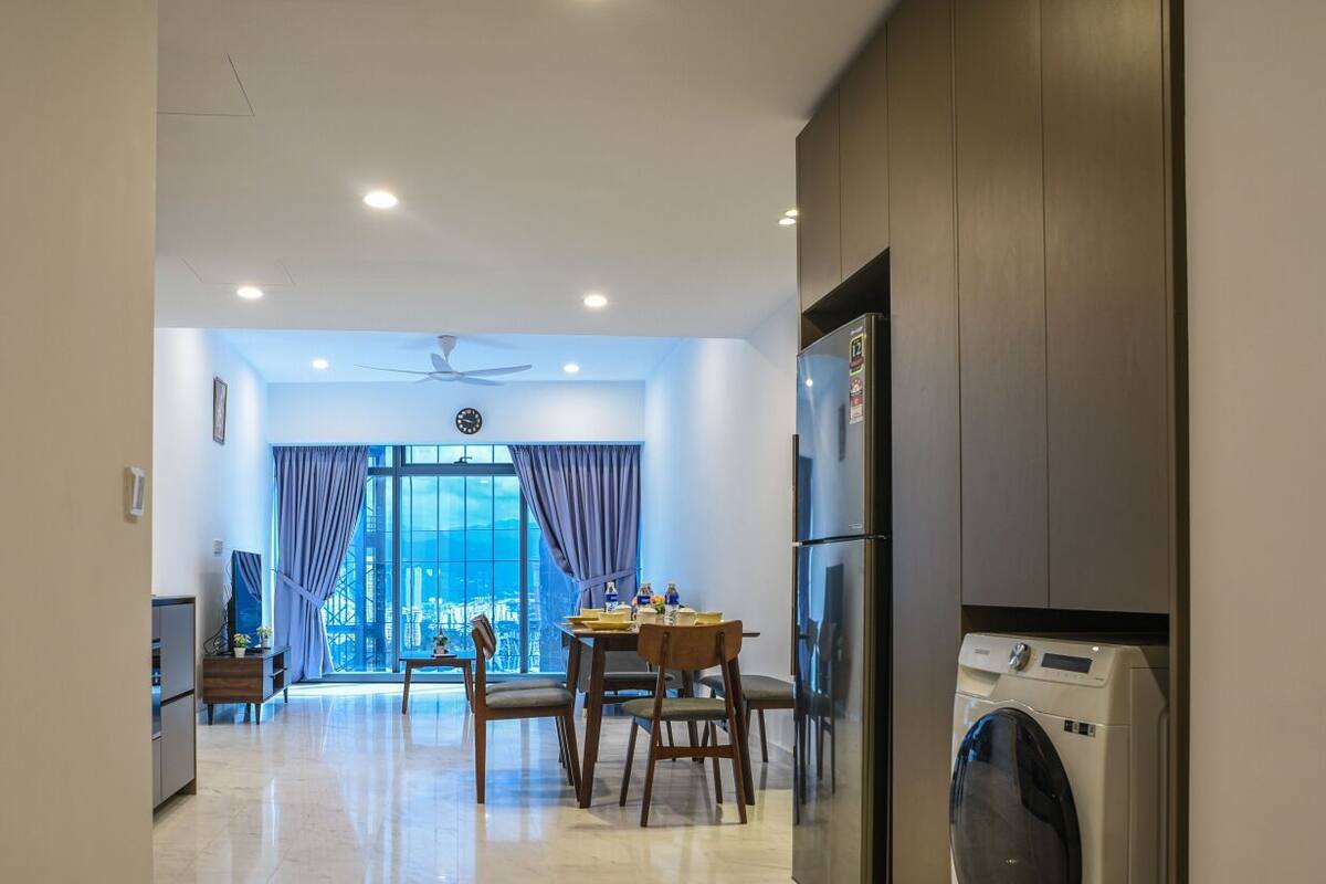 Una cocina moderna con lavadora incorporada, un comedor con mesa y sillas, y un amplio ventanal con cortinas.