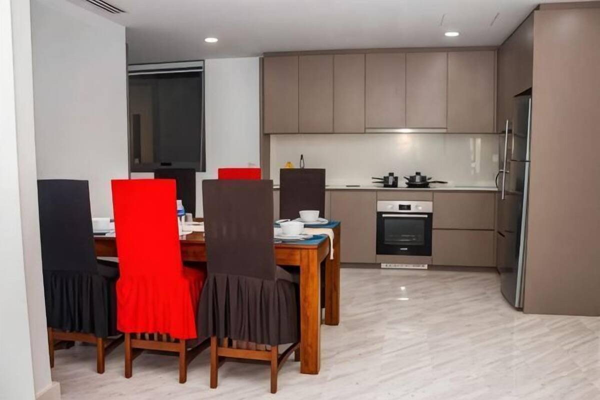 Una cocina compacta con electrodomésticos modernos, un comedor con sillas rojas y una pequeña mesa.