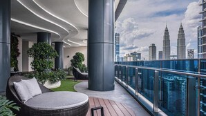 Un balcón moderno con vistas a las Torres Petronas, que incluye un sofá redondo de mimbre y plantas en macetas.