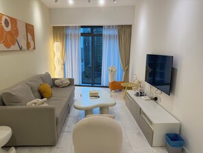 Un salon moderne avec un canapé, une table basse, un téléviseur et une grande fenêtre avec des rideaux.