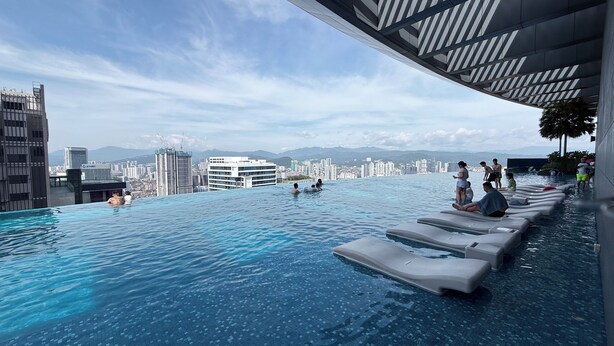 Piscina infinita en la azotea con vistas a la ciudad, sillas de descanso y un diseño arquitectónico moderno.