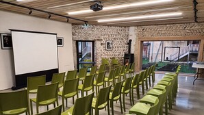 A conference room with rows of green chairs, a whiteboard, and a stone wall. - La ferme de Berlioz (La Cote-Saint-Andre)