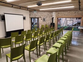A conference room with rows of green chairs, a whiteboard, and a stone wall.