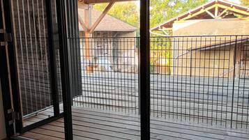 A room with a large window, wooden ceiling beams, and a view of an outdoor area with a fence and buildings.