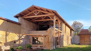 A rustic stone building with a wooden roof structure, large windows, and a grassy yard. - La ferme de Berlioz (La Cote-Saint-Andre)