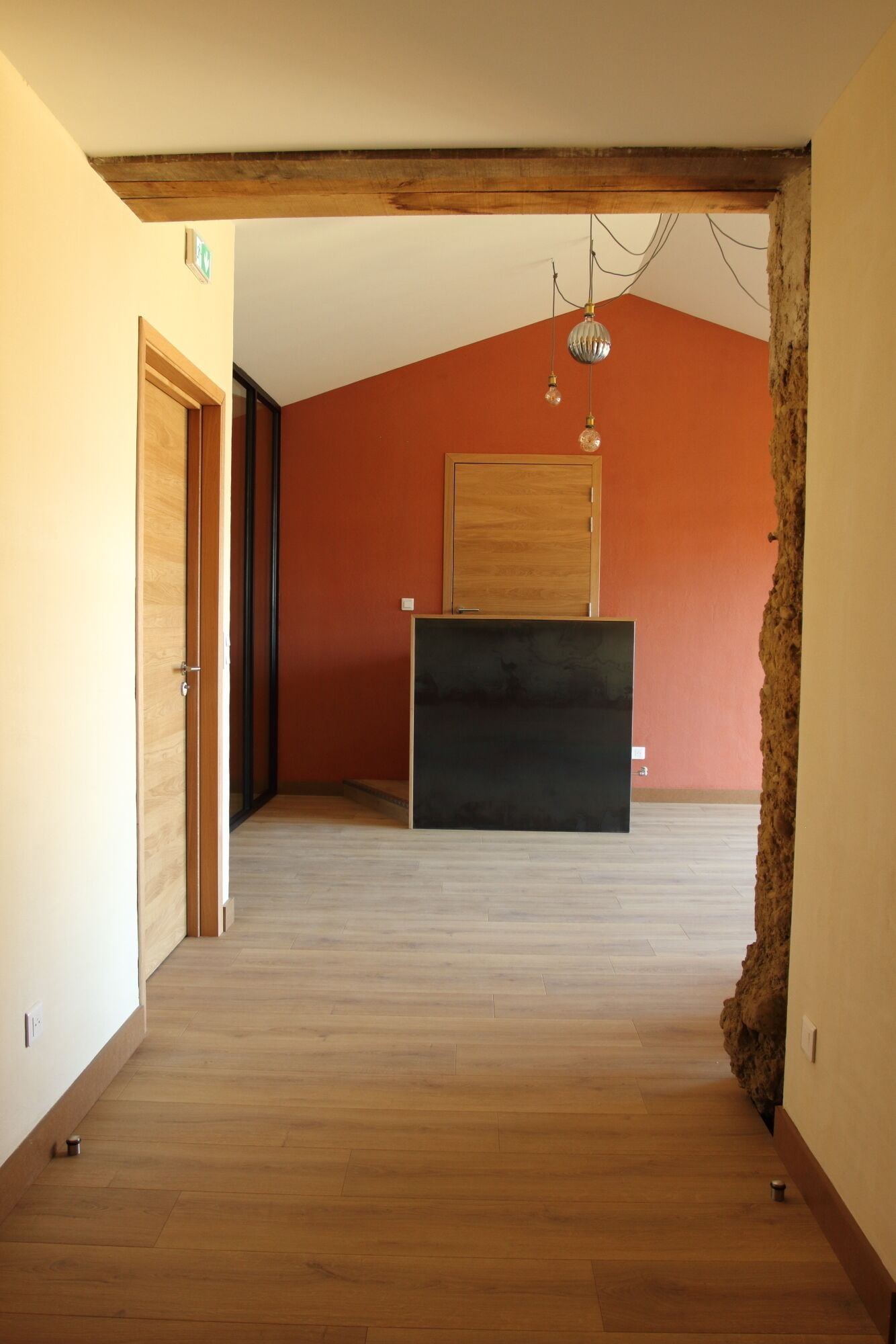 A hallway with wooden flooring, a wooden ceiling beam, and a black cabinet against a red wall.