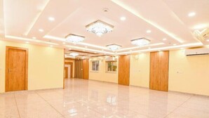 A spacious hotel lobby with a polished marble floor, wooden doors, and recessed lighting.