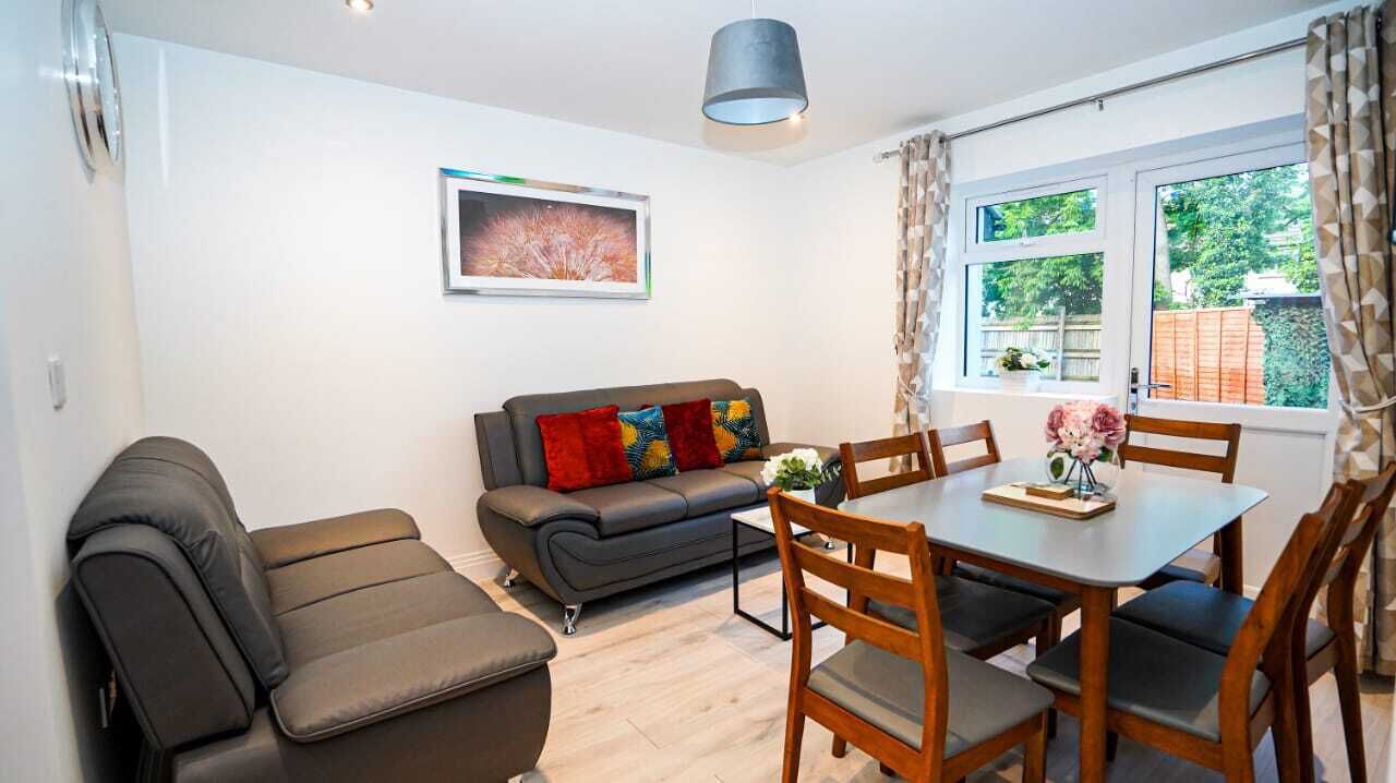A modern living room with a sofa, a dining table, and chairs. There is a window with curtains and a picture on the wall.