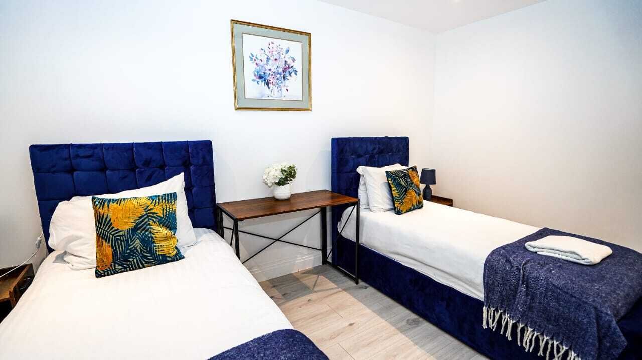 A hotel room with two beds, a small table, and a framed picture on the wall.