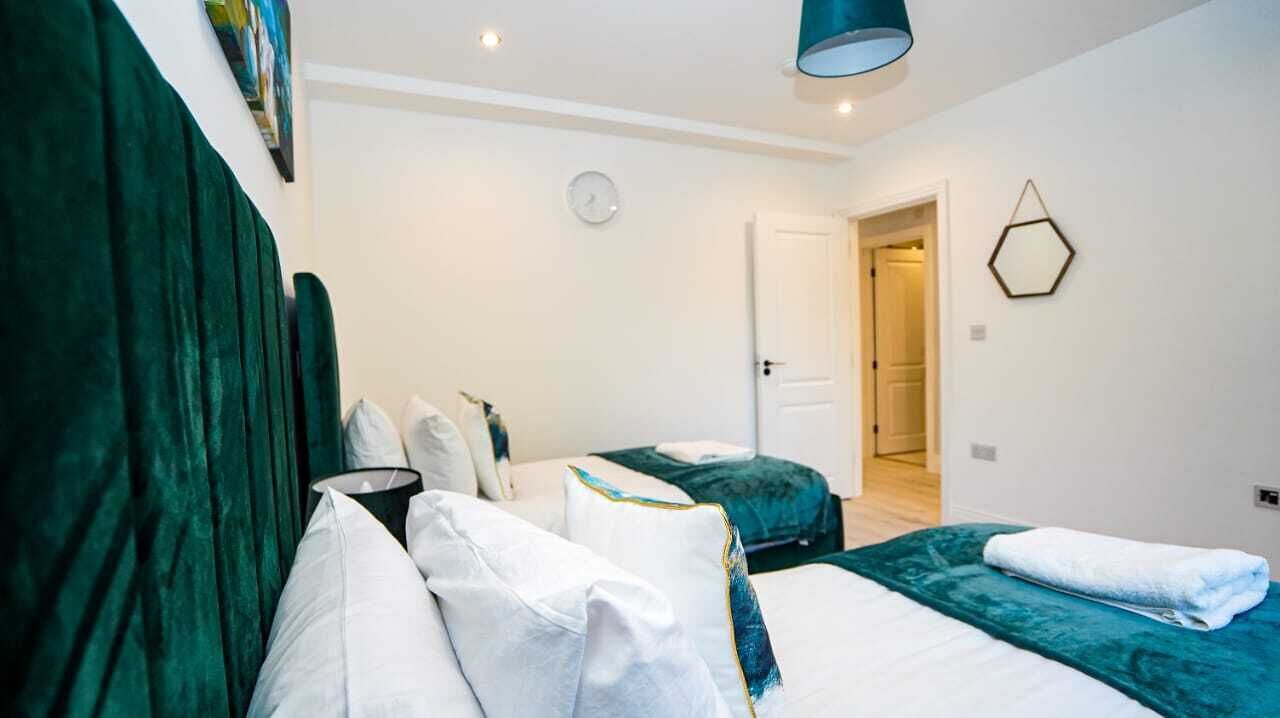 A hotel room with two beds, a green headboard, a clock, and a hexagonal wall decoration.