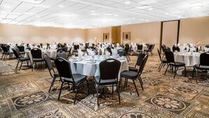 Un salón de conferencias con mesas redondas, sillas negras y alfombra estampada.
