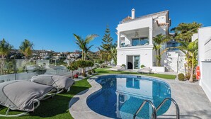 A modern villa with a swimming pool, a covered outdoor seating area, and a view of the surrounding neighborhood.