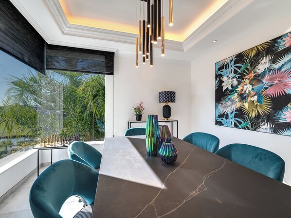 A modern dining area with a large table, teal chairs, and a view of greenery outside.