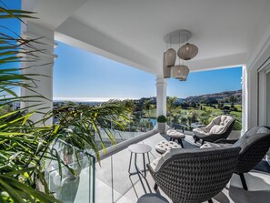 A balcony with wicker furniture, a glass railing, and a view of a green landscape.