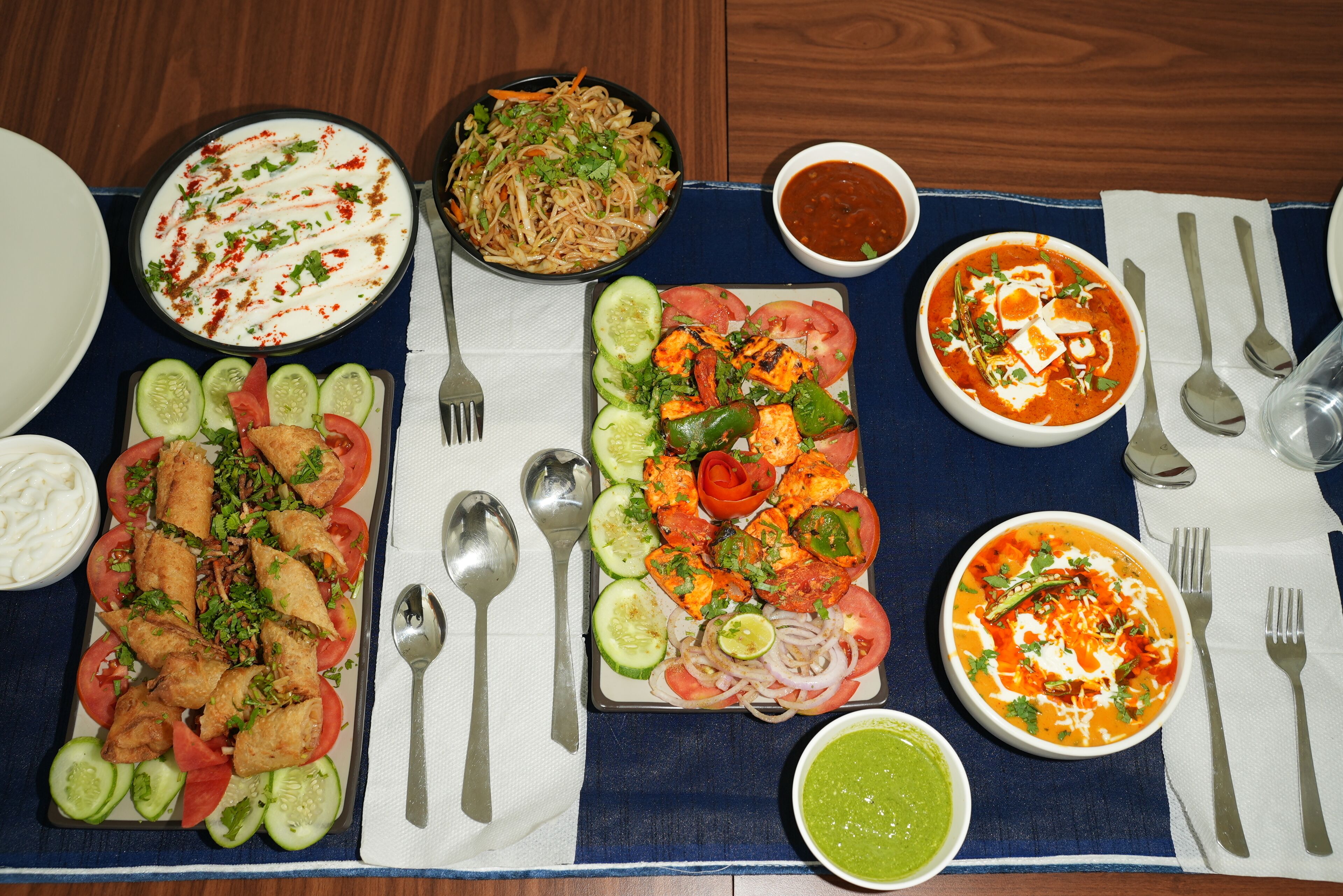 A table with various dishes including a salad, grilled vegetables, paneer, and a bowl of soup.