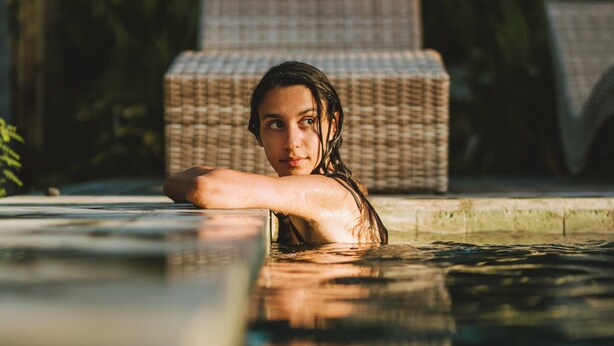 Una persona en una piscina con sillones de mimbre al fondo.
