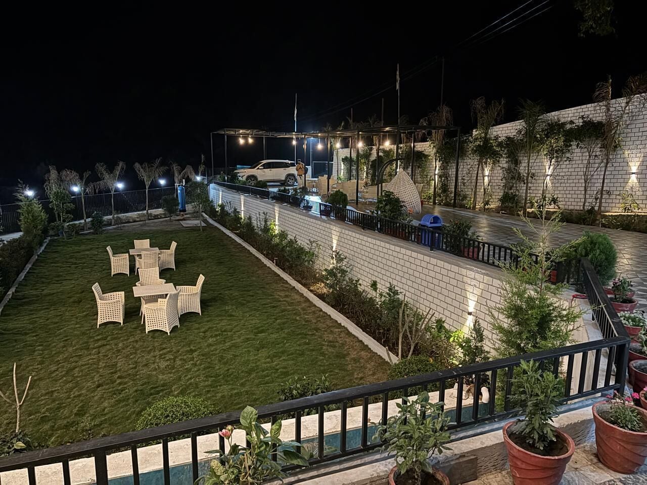 A well-lit outdoor area with a lawn, seating, and potted plants.
