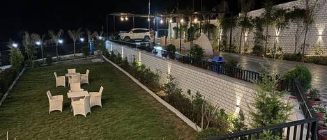 A well-lit outdoor area with a lawn, seating, and potted plants.