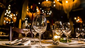 Una mesa de comedor dispuesta con varias copas de vino, tenedores y platos, que sugiere un ambiente de cena formal.