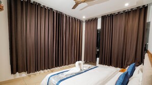 Una habitación de hotel con una cama grande, ventilador de techo y cortinas oscuras.