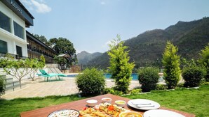 Una mesa de comedor con comida y una piscina al fondo.